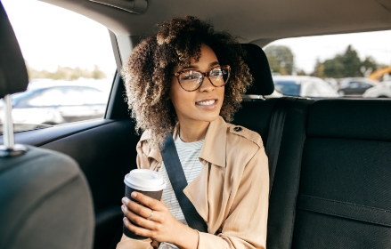 Woman in glasses in the back seat of a car holding a coffee